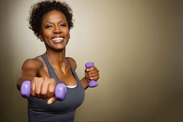 Black African lady working out with weights in grey top and a smile. Healthy living
