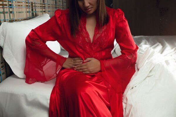Black lady in red dressing gown sitting on bed, experiencing internal heat - causes include gallstones or gall bladder inflammation