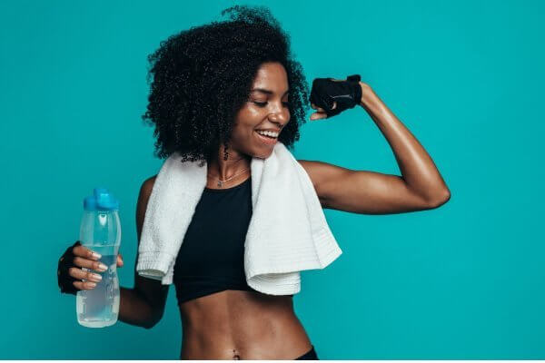 Looking pleased at kickstarting your fitness journey, photo shows a fit African lady showing off toned biceps and siling