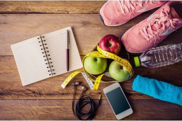 Planning, diet, time are some of the things you need to kickstart your fitness journey - photo shows diary, pen, phone, apples, water bottle, trainers and measuring tape