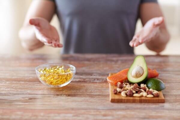 image of male hands displaying mixture of pills in a bowl and fruit and vegetable supplements on cutting board