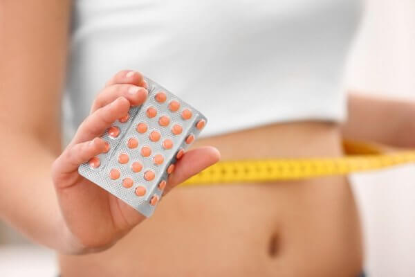 lady with a measuring tape around her waist holding a packet of birth control pills