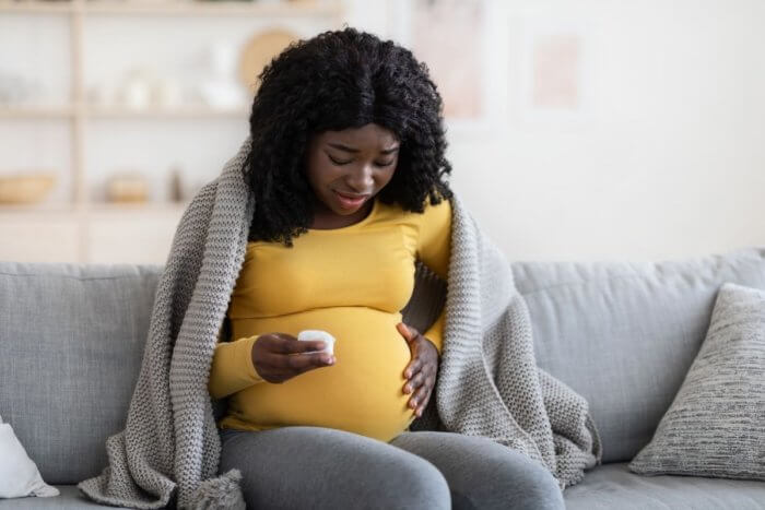 Pregnant young black lady in yellow jumper in image for postpartum bleeding